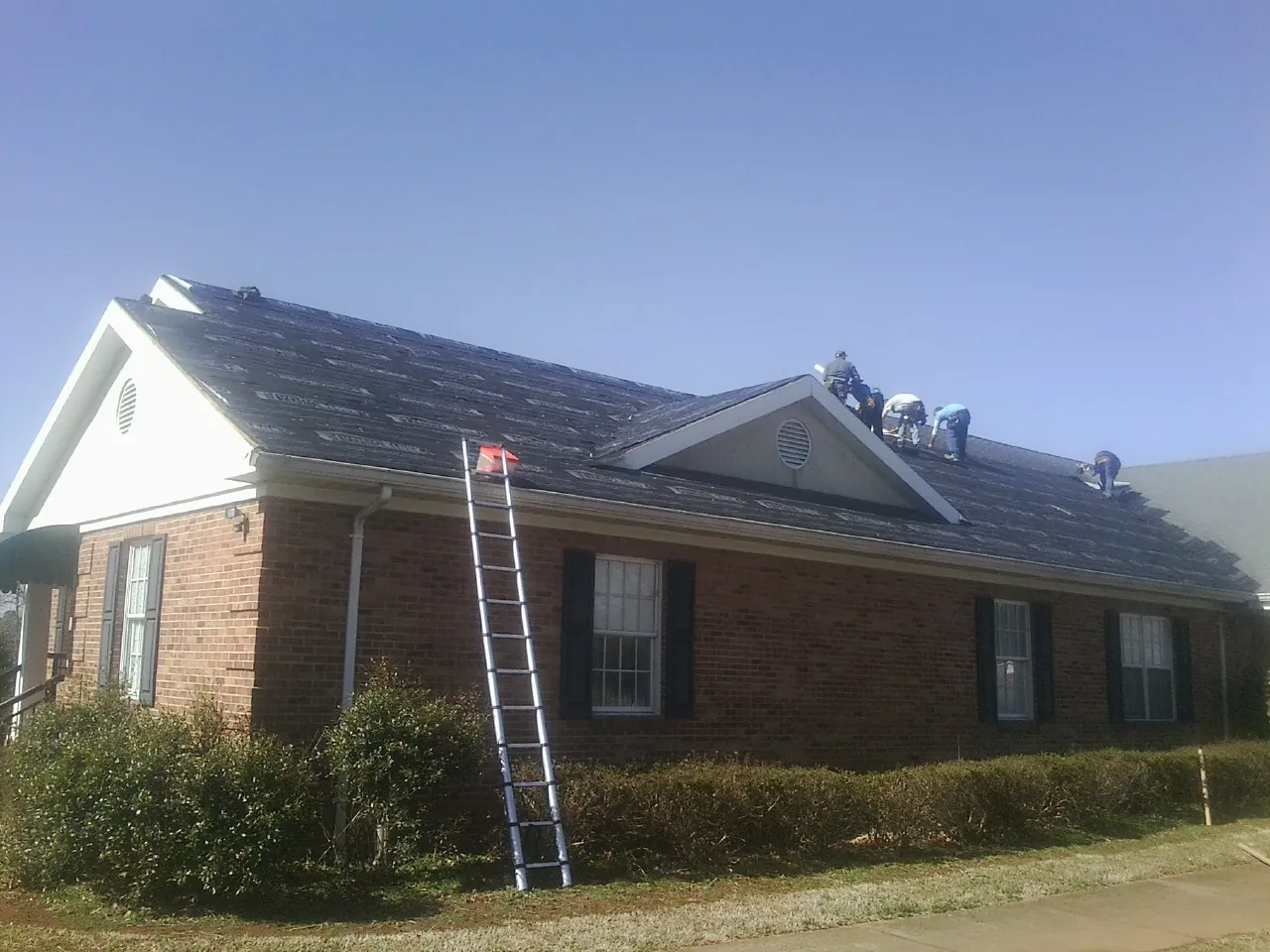 Crew tearing shingles off a brick ranch roof with a ladder set — Emergency Roof Repair work by our crew in Forest Ranch