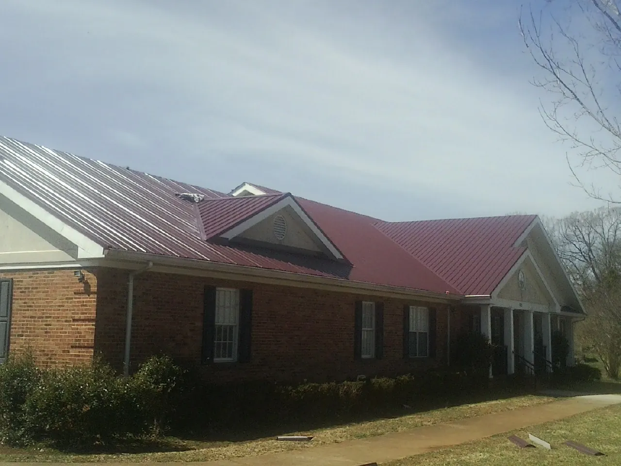 Red metal roof with gabled entries on a long brick building, from a Hail Damage Roof Repair job in Forest Ranch