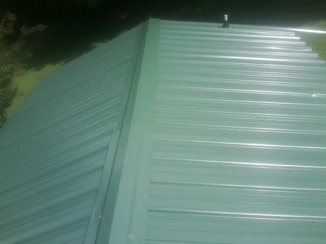 New green metal panels meeting at the ridge of a roof — Flat Roof Repair work by our crew in Forest Ranch
