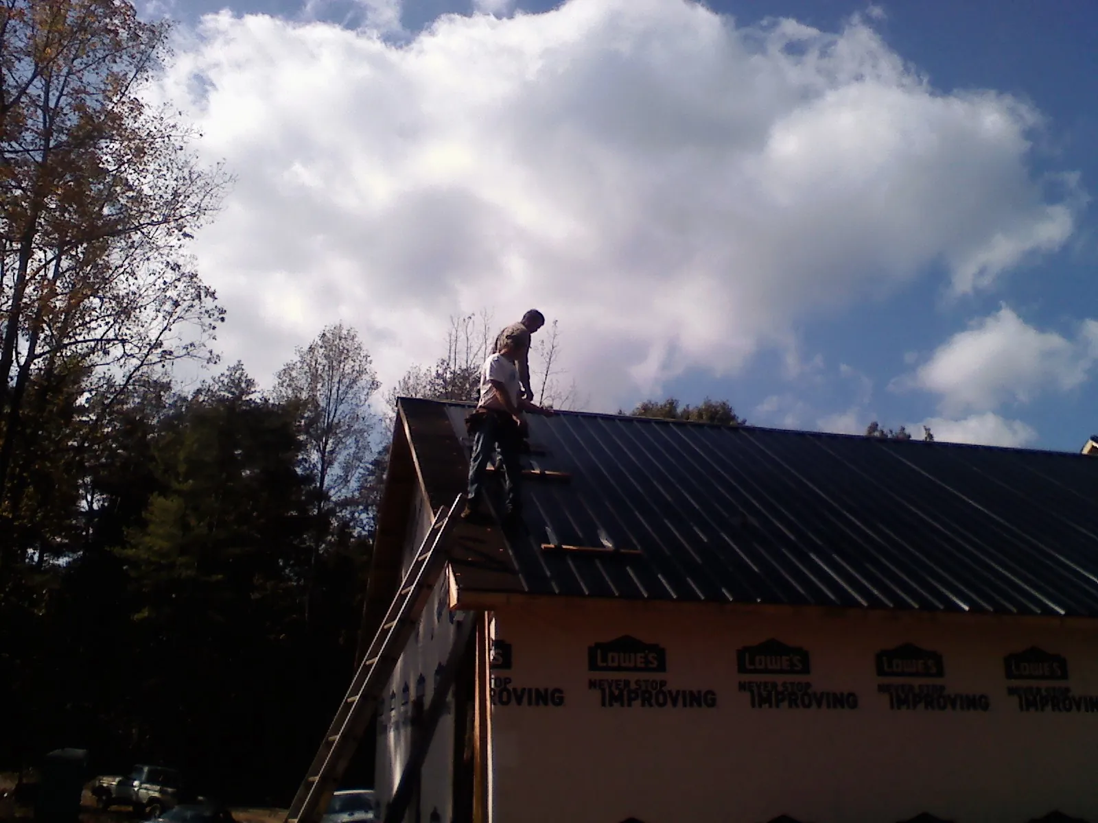 Roofer fastening dark metal panels high against a cloudy sky, from a Roof Inspection job in Forest Ranch